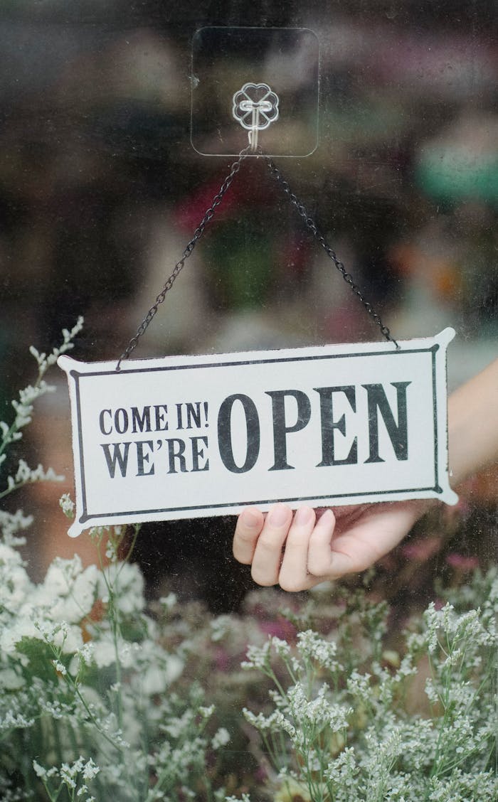 A welcoming open sign in a flower shop window with delicate blossoms in the foreground.