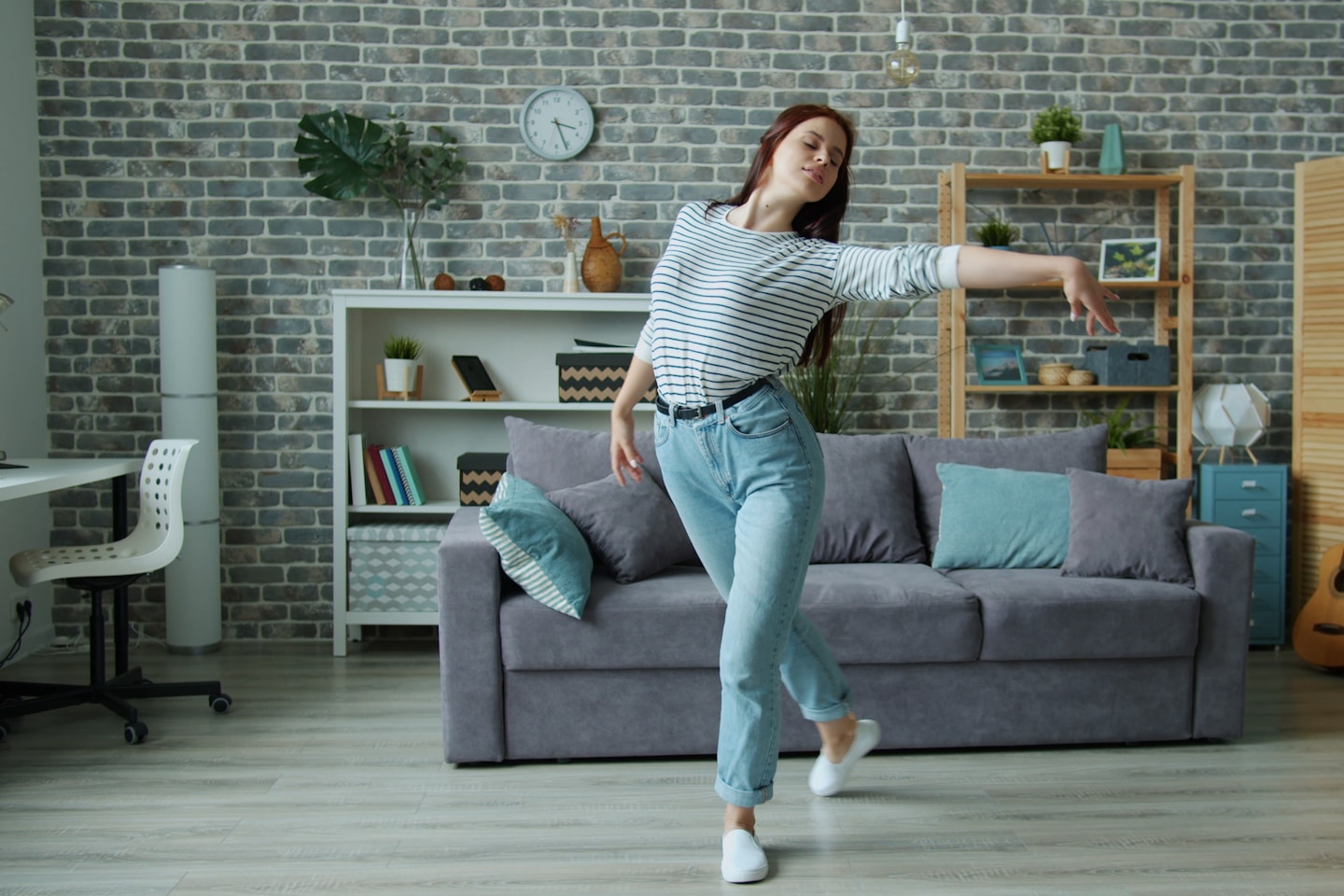 Beautiful young lady is dancing at home listening to music alone in cozy living room moving enjoying elegant dance. Apartment, interior and hobby concept.